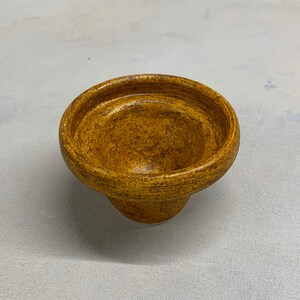 May include: A small, brown ceramic bowl with a speckled glaze. The bowl has a wide, rounded base and a slightly flared rim.