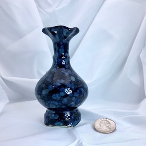 May include: A small, dark blue ceramic vase with a speckled glaze. The vase has a rounded body and a flared opening.