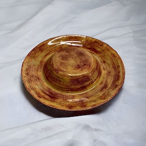 May include: A yellow and brown ceramic dish with a raised center. The dish has a rustic, handmade look.