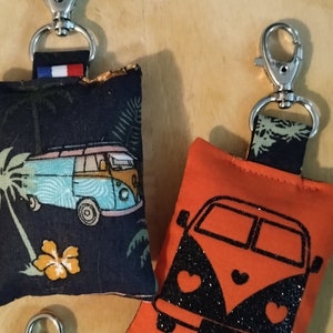 Peut inclure: Deux porte-clés avec des pochettes en tissu. Une pochette est noire avec un motif blanc et bleu d'un van et de palmiers. L'autre pochette est orange avec un motif de van noir. Les deux porte-clés ont des fermoirs en métal argenté.