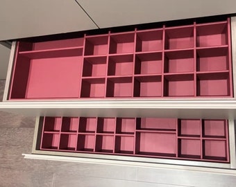 May include: Two open drawers with pink dividers. The top drawer has a large compartment and smaller compartments. The bottom drawer has smaller compartments.