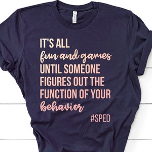 May include: Navy blue t-shirt with the text "IT'S ALL fun and games UNTIL SOMEONE FIGURES OUT THE FUNCTION OF YOUR behavior #SPED" in pink and white lettering.