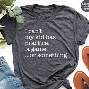 May include: A heather dark grey t-shirt with the text "I can't. My kid has practice. A game...or something" printed in white.