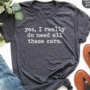 May include: Heather dark grey t-shirt with the text "yes, I really do need all these cars." printed in white.