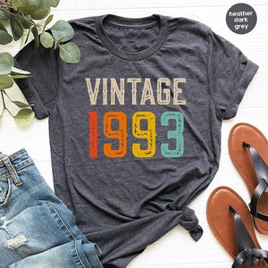 May include: Heather dark grey t-shirt with the text "Vintage 1993" in colorful, distressed lettering.