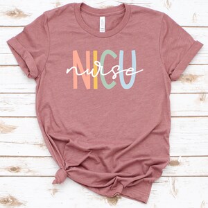 May include: A mauve t-shirt with the text "NICU nurse" in rainbow colors.