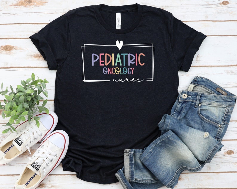 Peut inclure: Un t-shirt noir avec un cadre blanc et un c&oelig;ur. Le texte &agrave; l'int&eacute;rieur du cadre est "PEDIATRIC ONCOLOGY nurse" en couleurs arc-en-ciel.