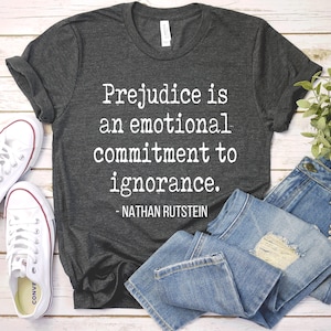 May include: A dark gray t-shirt with the quote "Prejudice is an emotional commitment to ignorance. - Nathan Rutstein" printed in white.