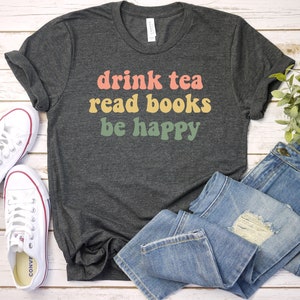 May include: A dark gray t-shirt with the text "drink tea read books be happy" in colorful retro font.