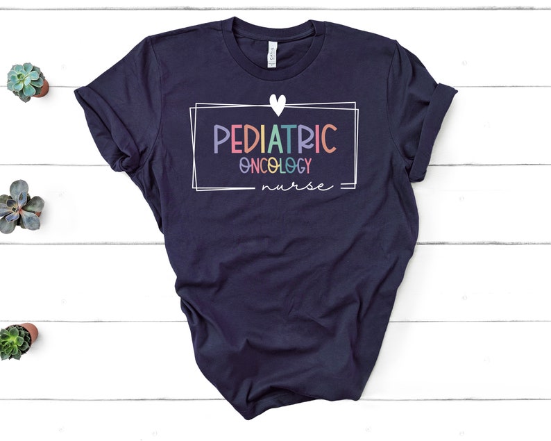 Peut inclure: Un t-shirt bleu marine avec un c&oelig;ur blanc et un cadre blanc autour du texte "PEDIATRIC ONCOLOGY nurse". Le texte est en couleurs arc-en-ciel.