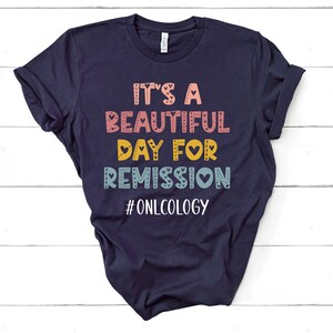 May include: Navy blue t-shirt with the text "It's a beautiful day for remission #oncology" in colorful letters with hearts.