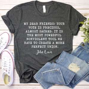 Pode incluir: Uma camiseta cinza escura com uma cita&ccedil;&atilde;o branca de John Lewis: "Meus queridos amigos: Seu voto &eacute; precioso, quase sagrado. &Eacute; a ferramenta n&atilde;o violenta mais poderosa que temos para criar uma uni&atilde;o mais perfeita."