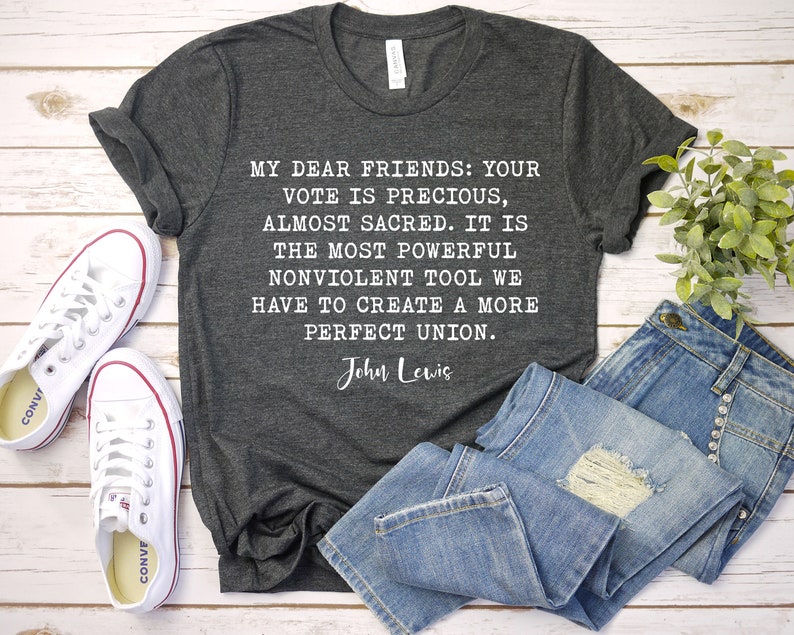 Pode incluir: Uma camiseta cinza escura com uma cita&ccedil;&atilde;o branca de John Lewis: "Meus queridos amigos: Seu voto &eacute; precioso, quase sagrado. &Eacute; a ferramenta n&atilde;o violenta mais poderosa que temos para criar uma uni&atilde;o mais perfeita."