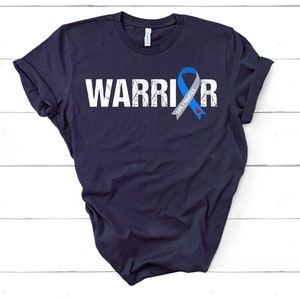 K&ouml;nnte beinhalten: Ein marineblaues T-Shirt mit dem Wort "WARRIOR" in wei&szlig; gedruckt und einem blauen und grauen Band mit dem Text "AWAREness" darauf.