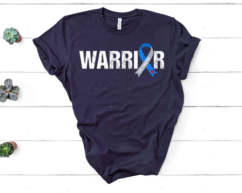 K&ouml;nnte beinhalten: Ein marineblaues T-Shirt mit dem Wort "WARRIOR" in wei&szlig; gedruckt und einem blauen und grauen Band mit dem Text "AWAREness" darauf.