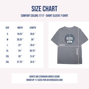 以下が含まれることがあります： Comfort Colors 1717半袖Tシャツのサイズチャート。Sから3XLまでのサイズと、インチ単位の幅と丈が記載されています。God Bless This Designと書かれた円形のグラフィックが入ったグレーのTシャツが、測定線と共に表示されています。
