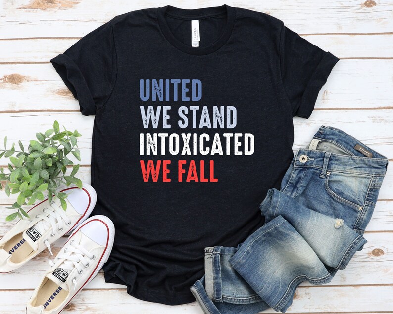 May include: A black t-shirt with the text "UNITED WE STAND INTOXICATED WE FALL" in blue, white, and red. The shirt is paired with blue jeans and white sneakers.