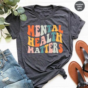 May include: A heather dark grey t-shirt with the text "Mental Health Matters" in colorful retro-style lettering.