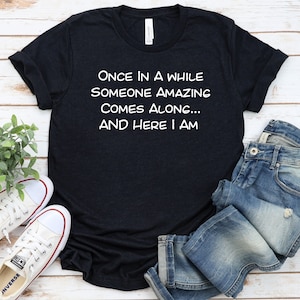 Peut inclure: Un t-shirt bleu fonc&eacute; avec du texte blanc qui dit "Once in a while someone amazing comes along... and here I am".