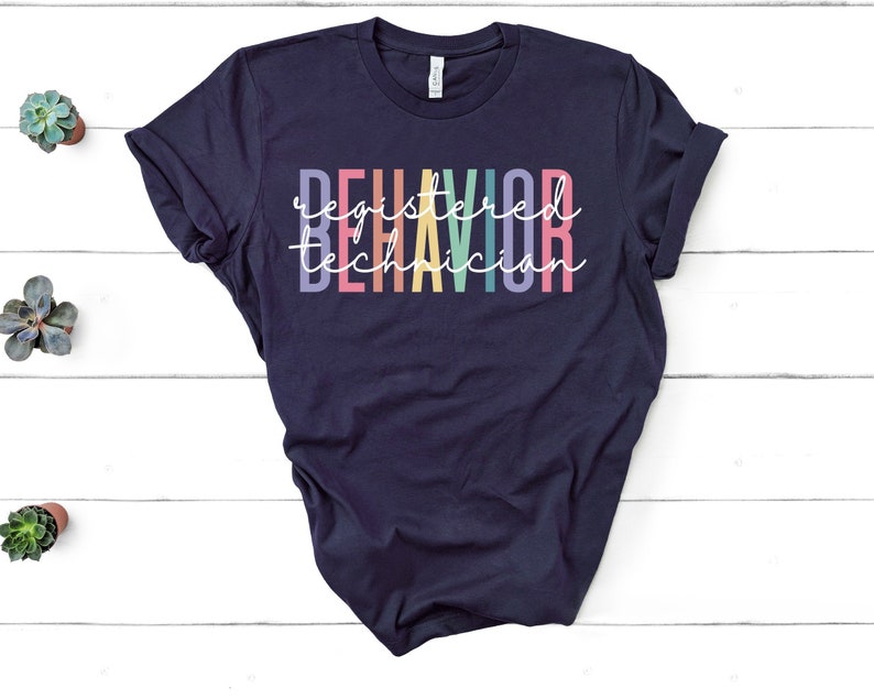 Puede incluir: Una camiseta azul marino con el texto "Registered Behavior Technician" en colores arco&iacute;ris.