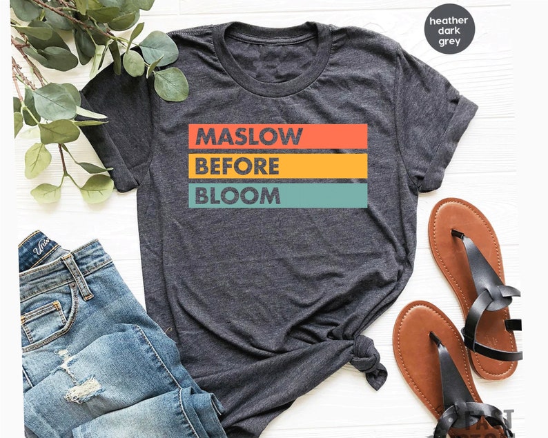 May include: Heather dark grey t-shirt with the text "Maslow Before Bloom" in a retro rainbow color scheme.