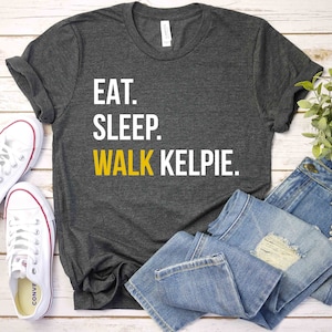 May include: A dark gray t-shirt with the text "EAT. SLEEP. WALK KELPIE." in white and yellow lettering.