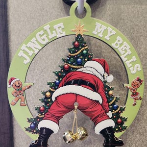 Könnte beinhalten: Ein kreisförmiger, hellgrüner Weihnachtsanhänger aus Holz mit dem Schriftzug JINGLE MY BELLS in weißen Buchstaben. Das Motiv zeigt einen geschmückten Weihnachtsbaum, zwei Lebkuchenfiguren und einen Weihnachtsmann mit zwei hängenden Goldglocken.