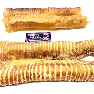 Può includere: Quattro snack per cani essiccati, di colore marrone chiaro, sono esposti su una superficie bianca. Gli snack hanno una consistenza a coste e una forma allungata. Sono di colore naturale e sembrano essere fatti di parti animali.