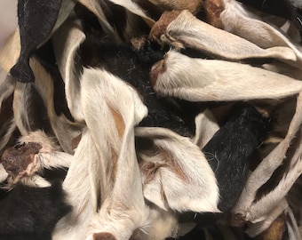 May include: A close-up of a pile of dried, raw, and natural dog treats. The treats are made of pig ears and are a variety of colors, including brown, white, and black.
