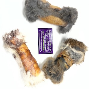 Könnte beinhalten: Drei rohe Leckerlis für Haustiere, darunter ein Knochen mit Fell und eine lila Visitenkarte. Die Leckerlis sind hellbraun, braun und grau. Die Visitenkarte trägt den Text "HEART SONG RAW PET FOOD" und eine Telefonnummer.