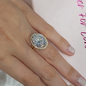 May include: A gold ring featuring a large oval-shaped diamond with a halo of smaller diamonds.