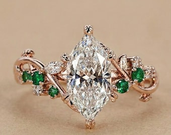May include: Rose gold ring featuring a marquise-cut diamond center stone. The ring is adorned with green emeralds and small white diamonds, set in a floral vine design. A beautiful piece of jewelry.
