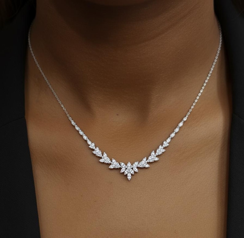 Puede incluir: Un delicado collar de plata con un dise&ntilde;o en forma de hojas. El collar presenta una serie de peque&ntilde;as piedras brillantes dispuestas en un patr&oacute;n sim&eacute;trico. El dise&ntilde;o central es un grupo de piedras, con una fina cadena.