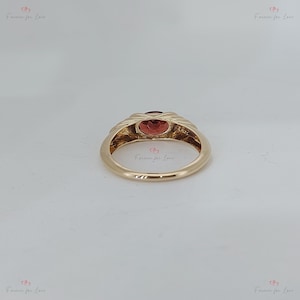 Puede incluir: Un anillo de oro con una piedra preciosa ovalada de color rojo anaranjado. La banda del anillo tiene un dise&ntilde;o texturizado y tejido alrededor de la piedra preciosa. El anillo est&aacute; sobre un fondo neutro. Las palabras "Forever for Love" est&aacute;n impresas en la imagen.