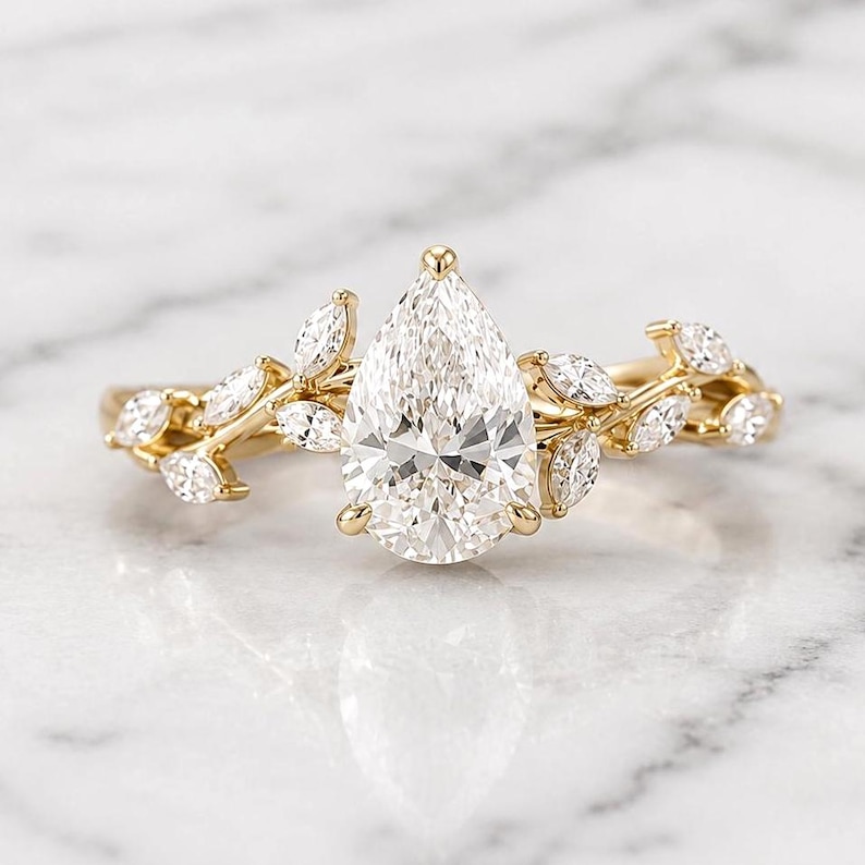 May include: A gold ring featuring a large, pear-shaped diamond as the centerpiece. The band is adorned with smaller, marquise-cut diamonds and a delicate leaf design, creating an elegant and nature-inspired aesthetic.