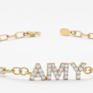 May include: A gold bracelet spelling out "AMY" in clear, sparkling gemstones. The bracelet has a chain-link design and a row of small, clear gemstones. A delicate and personalised piece of jewellery.
