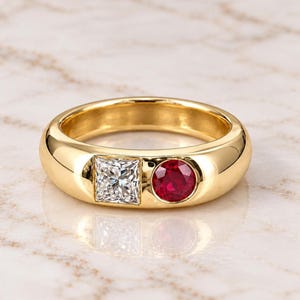 Puede incluir: Un anillo de banda de oro amarillo pulido que presenta una piedra preciosa transparente de corte princesa cuadrado engastada junto a una piedra preciosa roja vibrante de corte redondo. La banda tiene un perfil liso y redondeado con acabado brillante.