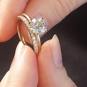 May include: A close-up of a gold wedding band set with a large, round, brilliant-cut diamond solitaire engagement ring. The band is set with smaller diamonds.