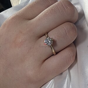May include: A gold engagement ring with a round, clear diamond center stone.