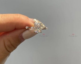 Puede incluir: Un anillo de plata con una gran piedra preciosa rectangular transparente. El anillo tiene pequeñas piedras preciosas transparentes a cada lado de la piedra principal.