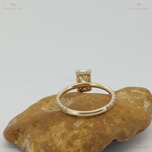 May include: A gold engagement ring with a square-shaped center stone and a halo of smaller stones. The band is set with smaller stones that continue around the entire ring.