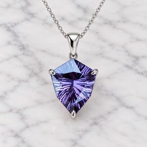 Könnte beinhalten: Eine silberne Anhängerkette mit einem schildförmigen, facettierten violetten und blauen Edelstein. Der Stein weist ein strahlenförmiges Schliffmuster auf und ist in einer dreizackigen Fassung an einer feinen Silberkette befestigt.