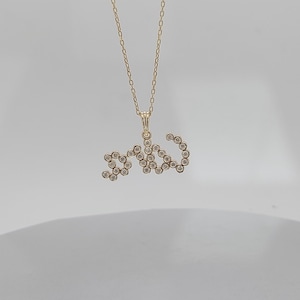 May include: Gold-coloured necklace featuring a pendant spelling "love" in a cursive script. The pendant and chain are delicate, with small gemstones set into the letters.