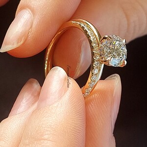 May include: A gold engagement ring with a large, round, clear diamond center stone. The ring has a thin band and a halo of smaller diamonds around the center stone.