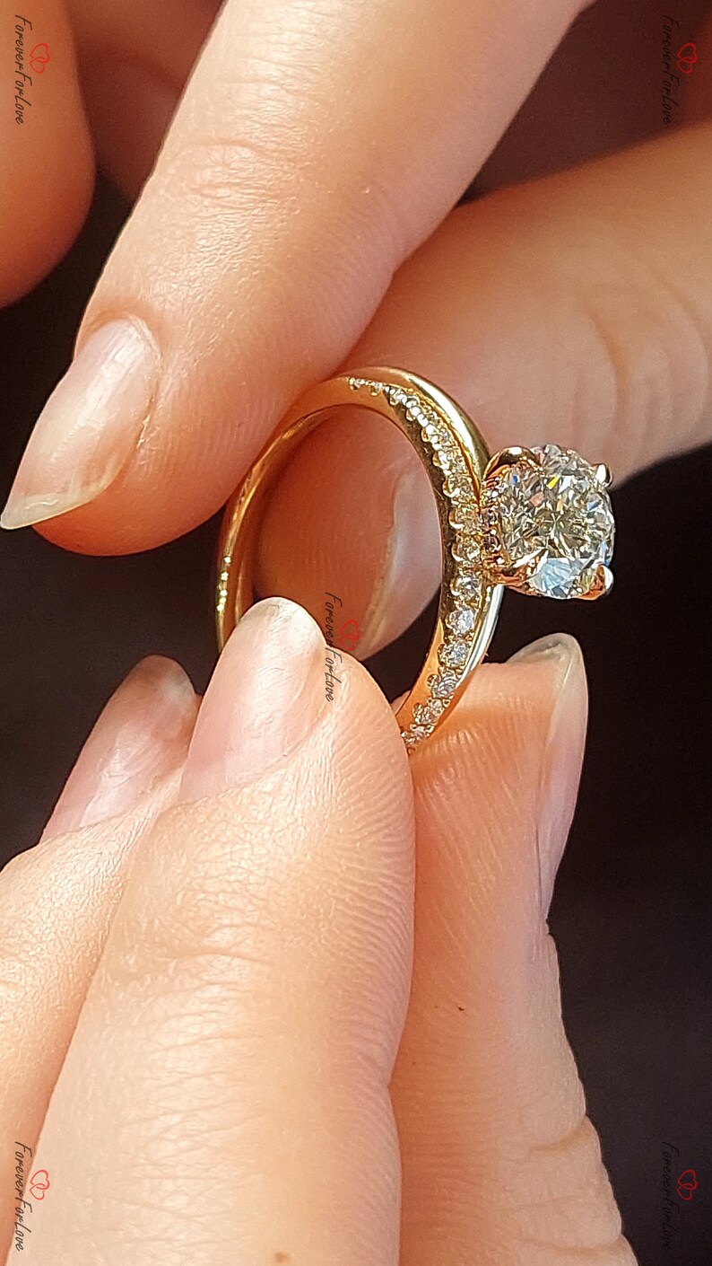 May include: A gold engagement ring with a large, round, clear diamond center stone. The ring has a thin band and a halo of smaller diamonds around the center stone.
