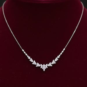 Puede incluir: Un delicado collar de plata con un dise&ntilde;o floral. El collar presenta una serie de peque&ntilde;as gemas brillantes dispuestas en un patr&oacute;n de hojas. El collar se exhibe sobre un fondo de terciopelo rojo oscuro.