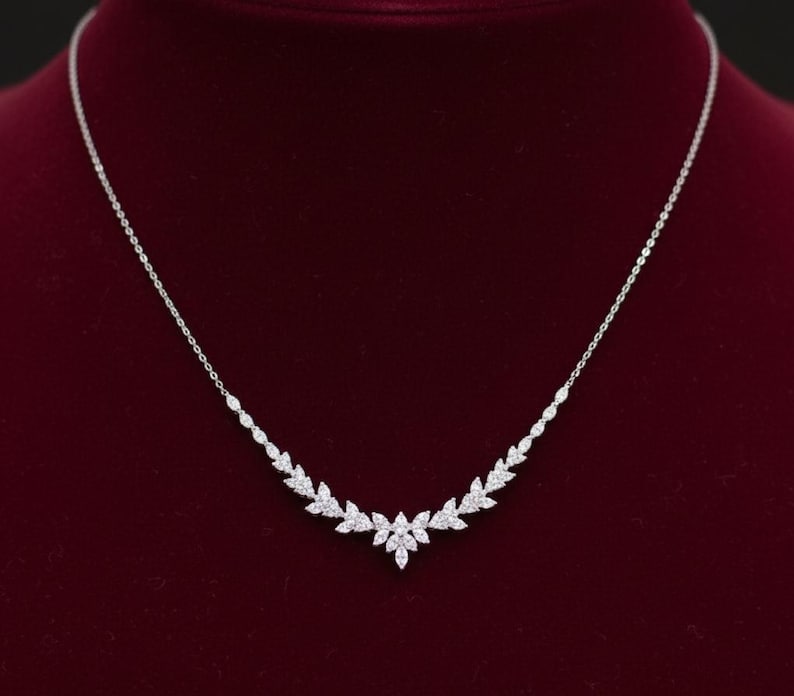 Puede incluir: Un delicado collar de plata con un dise&ntilde;o floral. El collar presenta una serie de peque&ntilde;as gemas brillantes dispuestas en un patr&oacute;n de hojas. El collar se exhibe sobre un fondo de terciopelo rojo oscuro.