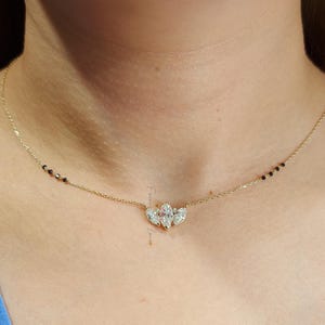May include: A gold chain necklace with a pendant featuring three marquise-shaped diamonds set in a flower-like design. The chain has black beads interspersed throughout.