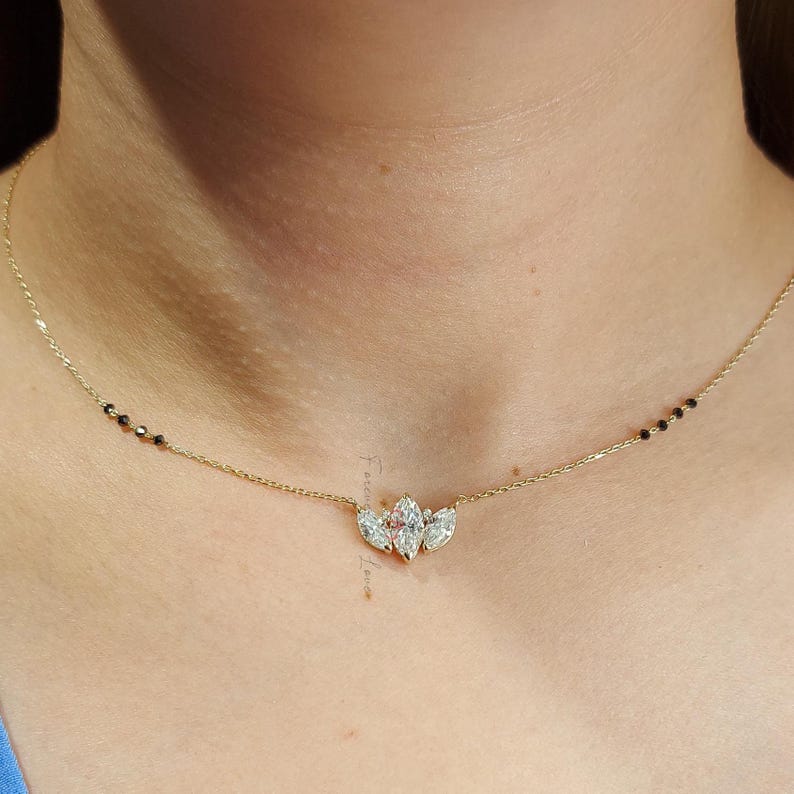 May include: A gold chain necklace with a pendant featuring three marquise-shaped diamonds set in a flower-like design. The chain has black beads interspersed throughout.