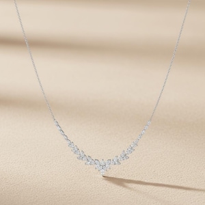 Puede incluir: Un delicado collar de plata con un dise&ntilde;o floral. El collar presenta una serie de peque&ntilde;as piedras brillantes dispuestas en un patr&oacute;n curvo, con un grupo central de piedras que forman un colgante. La cadena es fina y elegante.